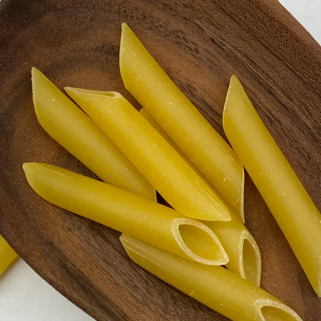 A close up shot of Penne in a wooden serving spoon