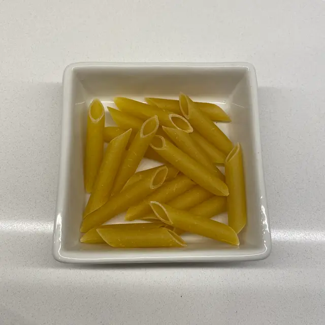 Penne in a square white glass bowl