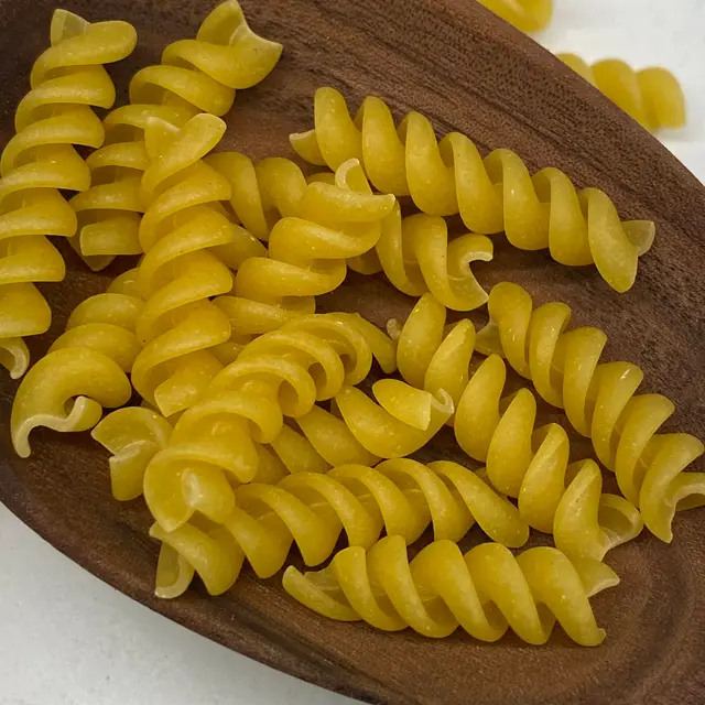 A close up shot of Rotini in a wooden serving spoon