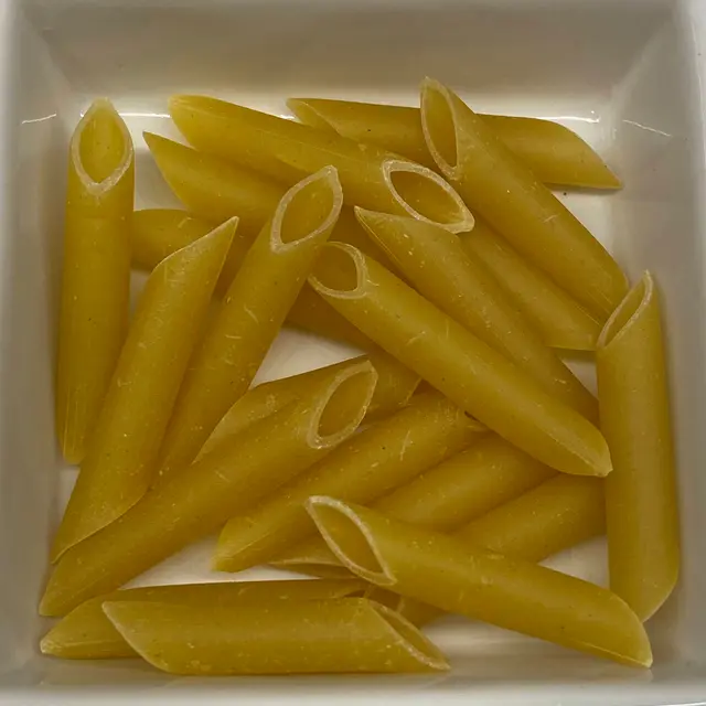 A close up shot of Penne in a square white glass bowl